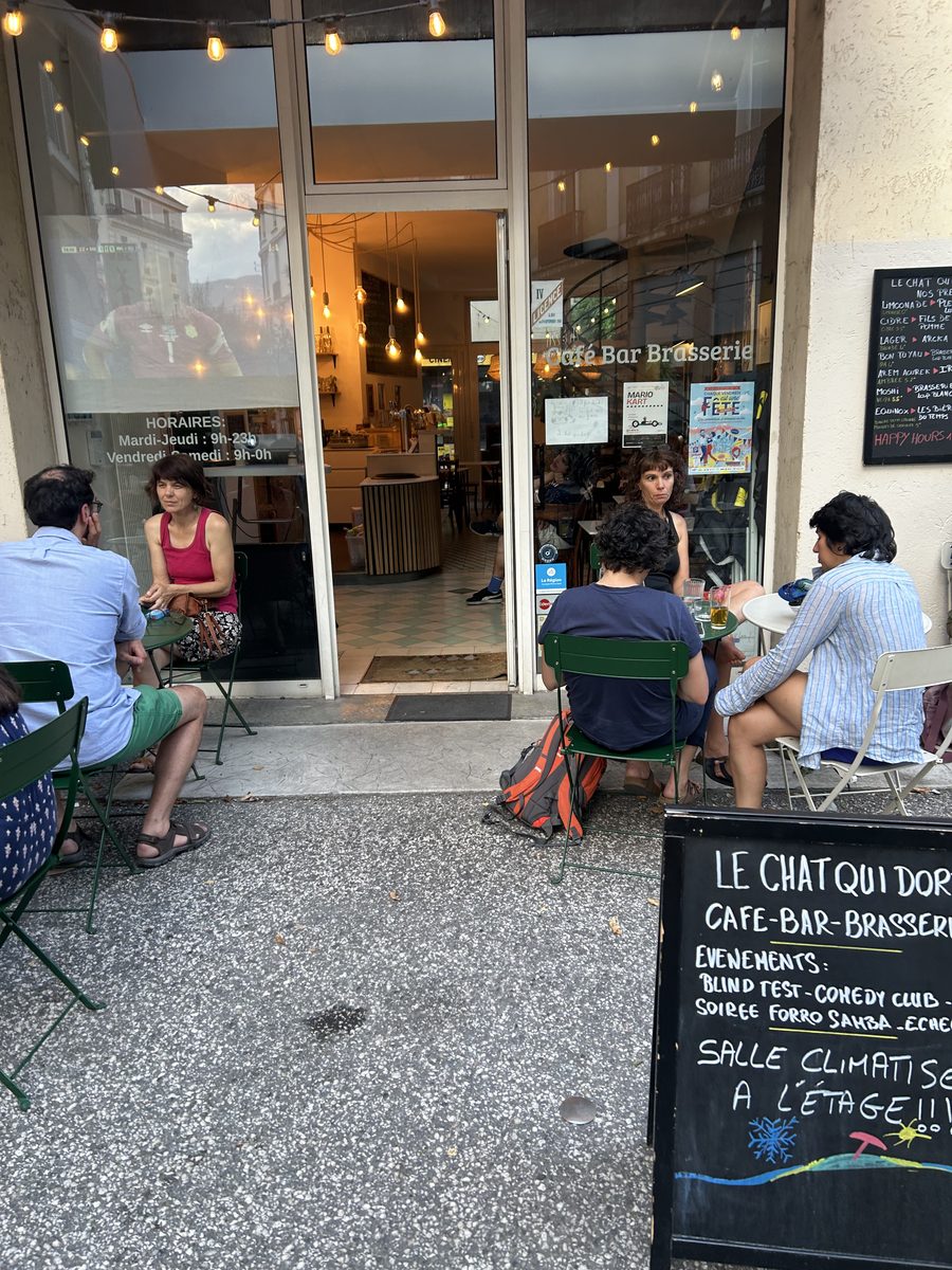 Clients en terrasse devant l'entrée, ardoise des événements de la semaine
