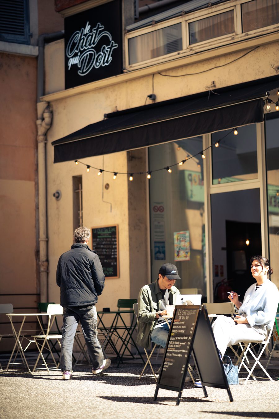 Clients en terrasse au soleil devant l'ardoise du Chat qui dort